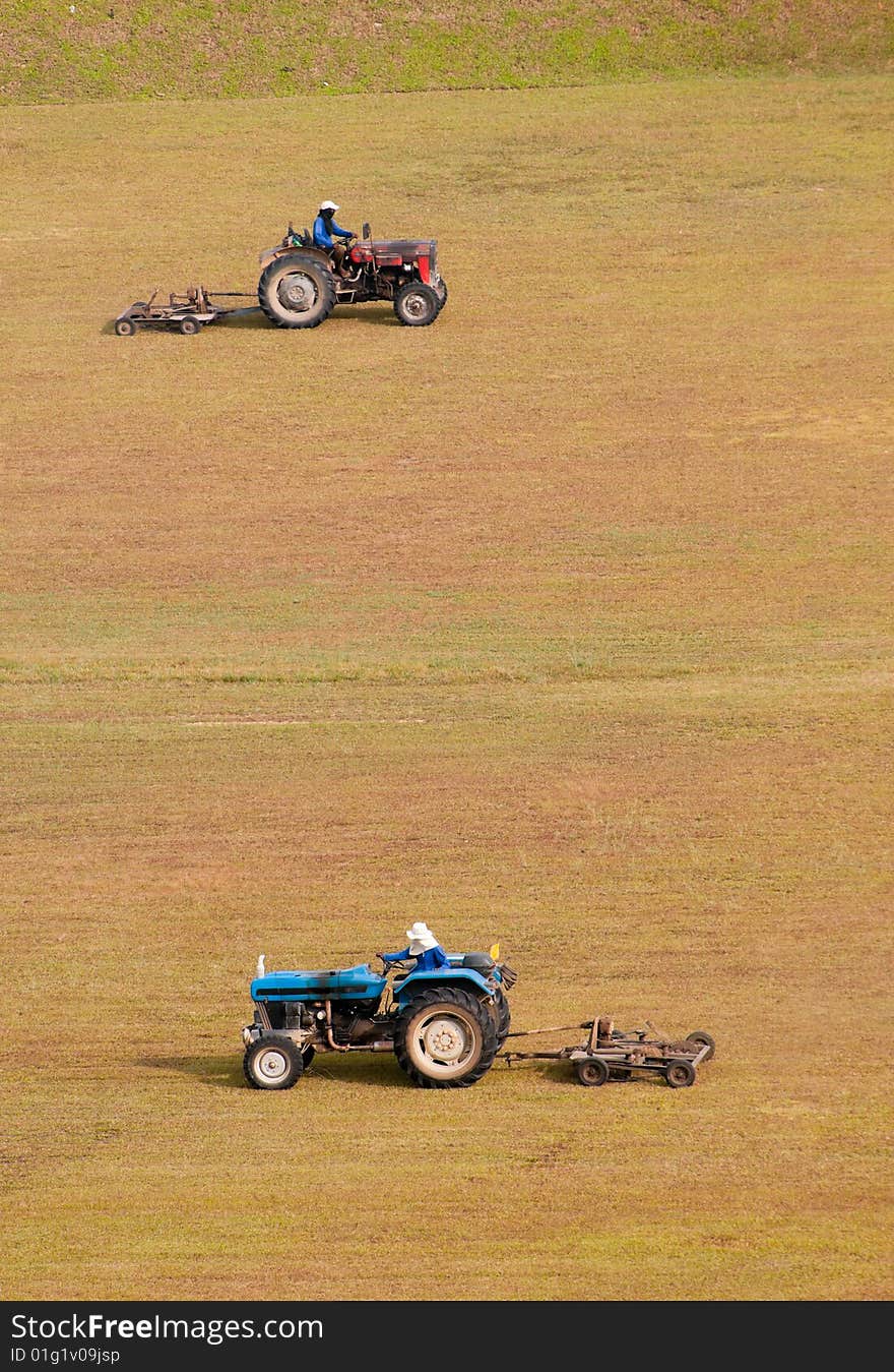 A pair of tractor-towed mowers moving a large open flat dry field. A pair of tractor-towed mowers moving a large open flat dry field