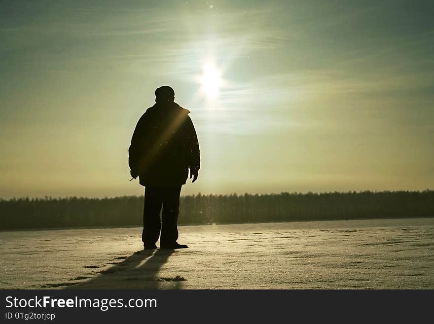 The person stands on a snow field under light of evening sun. The person stands on a snow field under light of evening sun