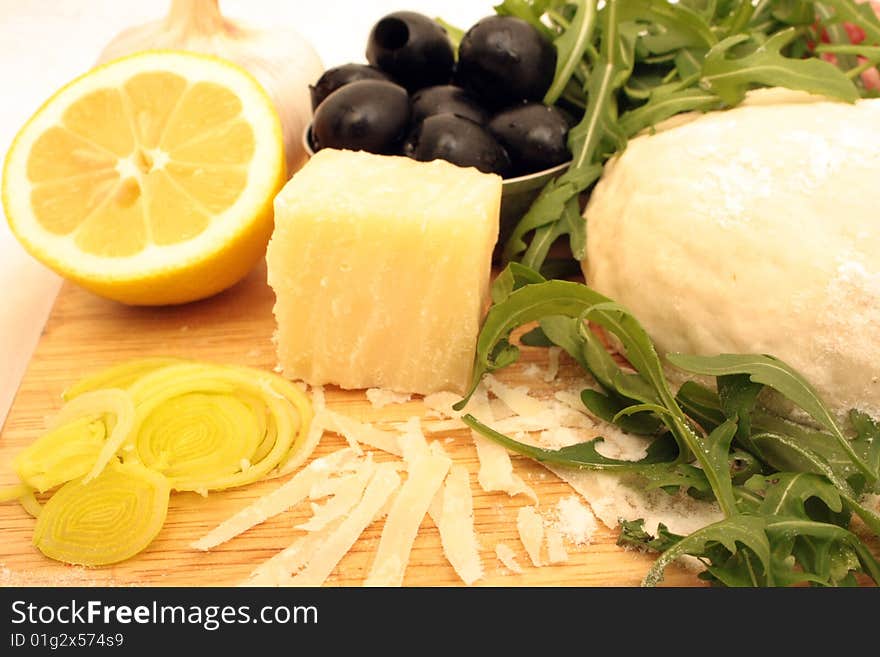 Pizza dough, olives, garlic, grana padano cheese, lemon and rukola on the board. Pizza dough, olives, garlic, grana padano cheese, lemon and rukola on the board.