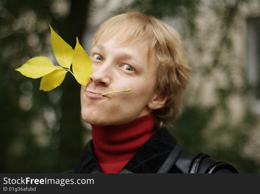 A young man with yellow autumn leaves in teeth