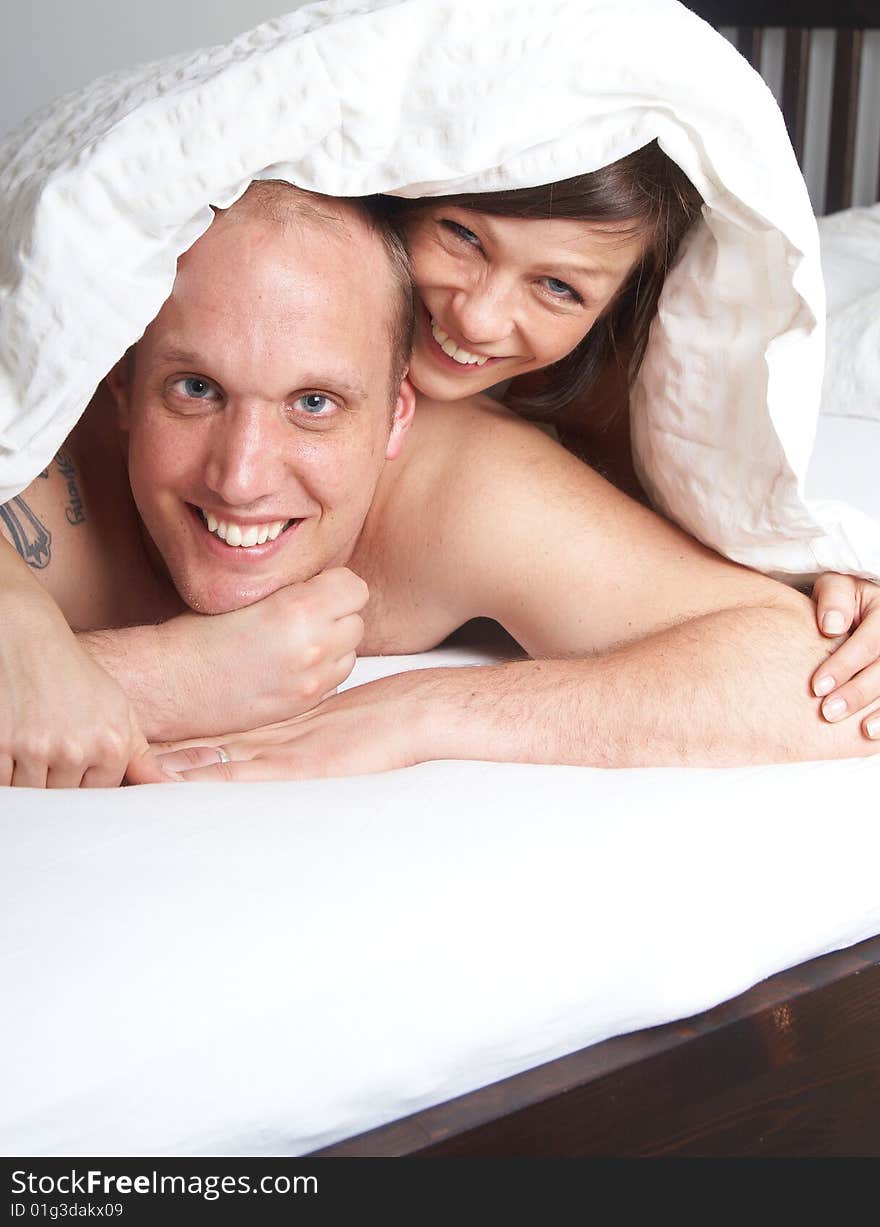 Young couple in their bed. They are playing in romance under the sheets.