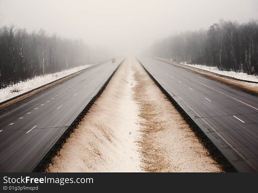 Snowy highway in the dark foggy forest