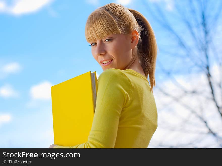 Beautiful blond girl with yelow book walking , looking back, Back To School