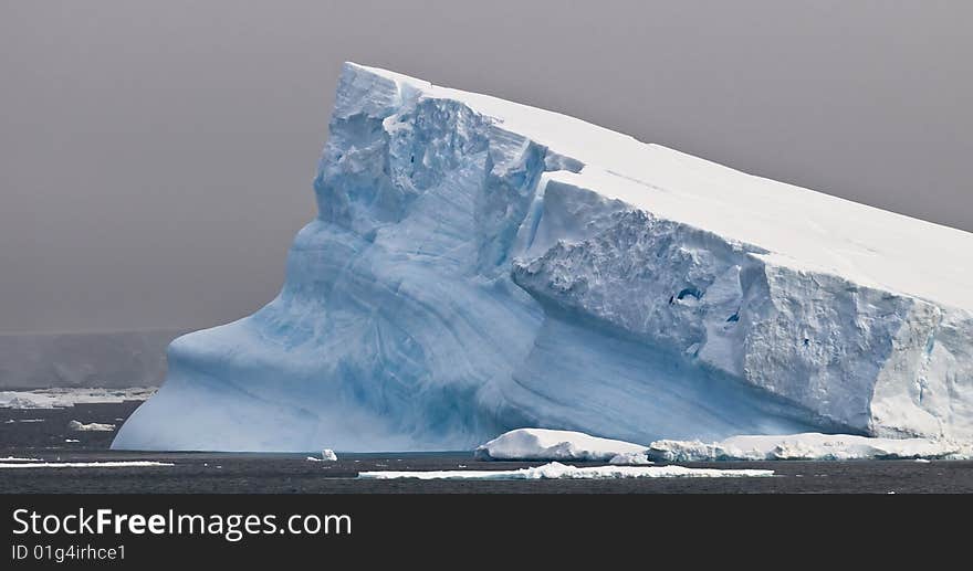 A huge tabular iceberg slanting into the sea in Antarctica. A huge tabular iceberg slanting into the sea in Antarctica.