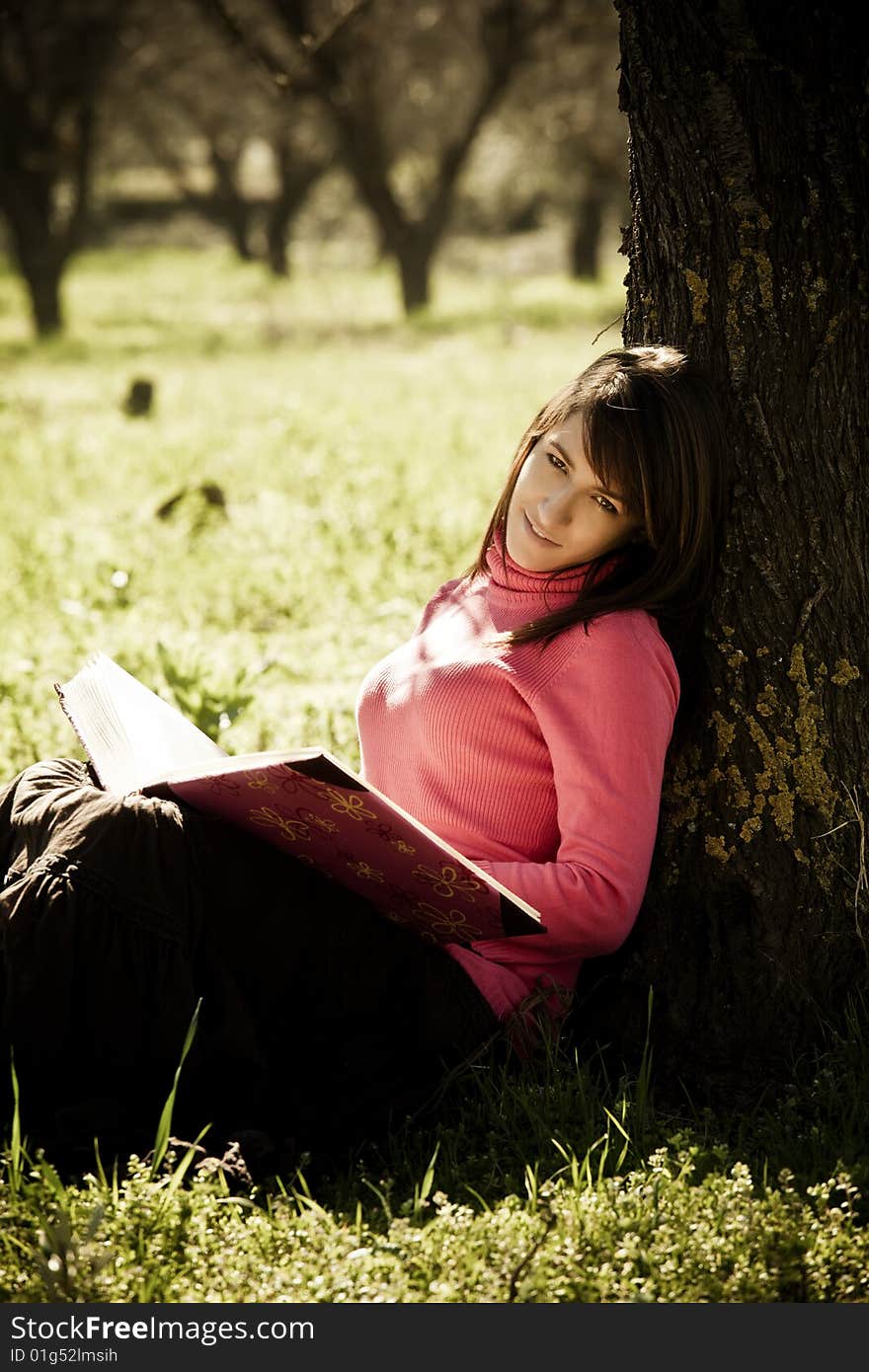 Young cheerful woman enjoying a book in the forest.