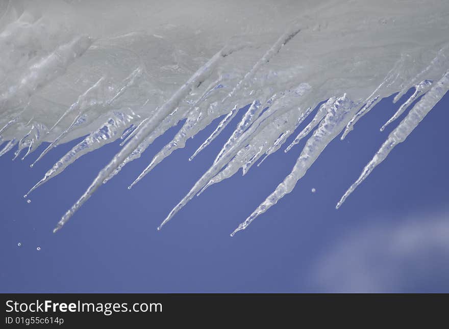 Icicles against a bright blue sky with drips of melting water