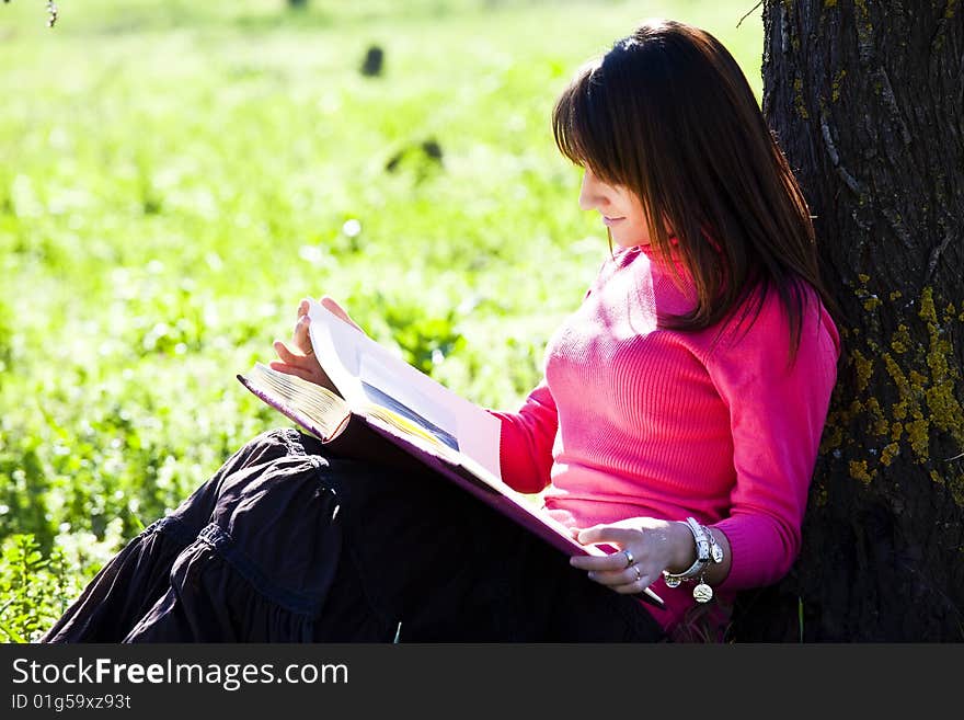 Young cheerful woman enjoying a book in the forest.