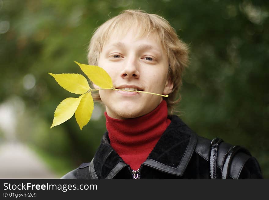 A young man with yellow autumn leaves in your teeth