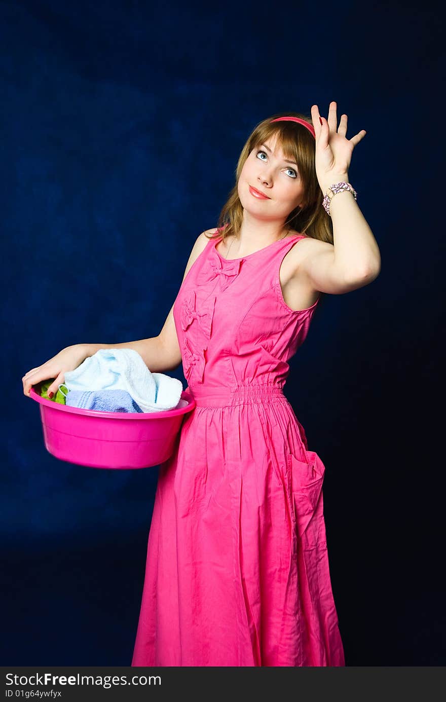 Charming young tired housewife with a basin full of clothes, against blue background