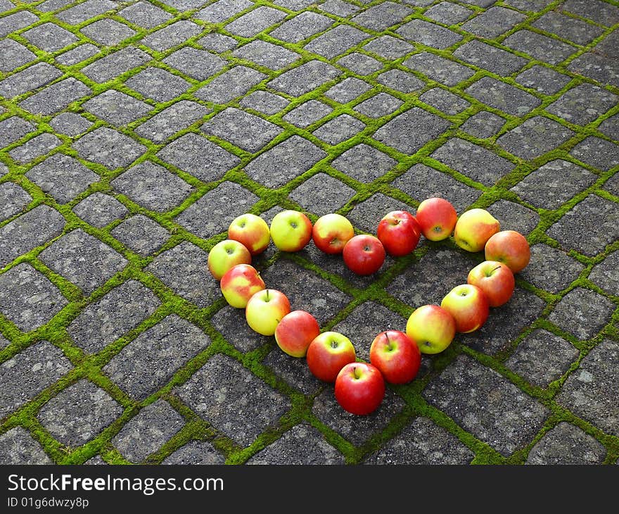 A heart of apples on road stones with moss. A heart of apples on road stones with moss