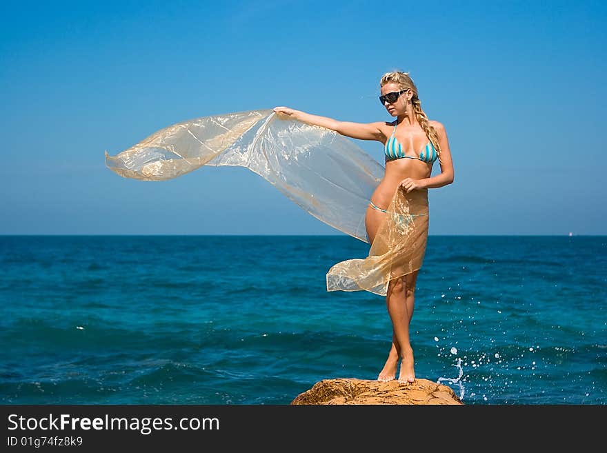 Beautiful girl in sunglasses and with transparent cloth standing on rocky beach. Beautiful girl in sunglasses and with transparent cloth standing on rocky beach