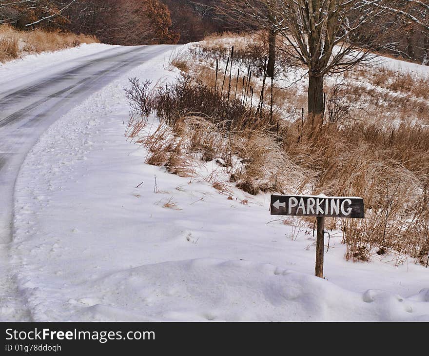 Wooden parking sign alongside a road in a park after a snowfall.