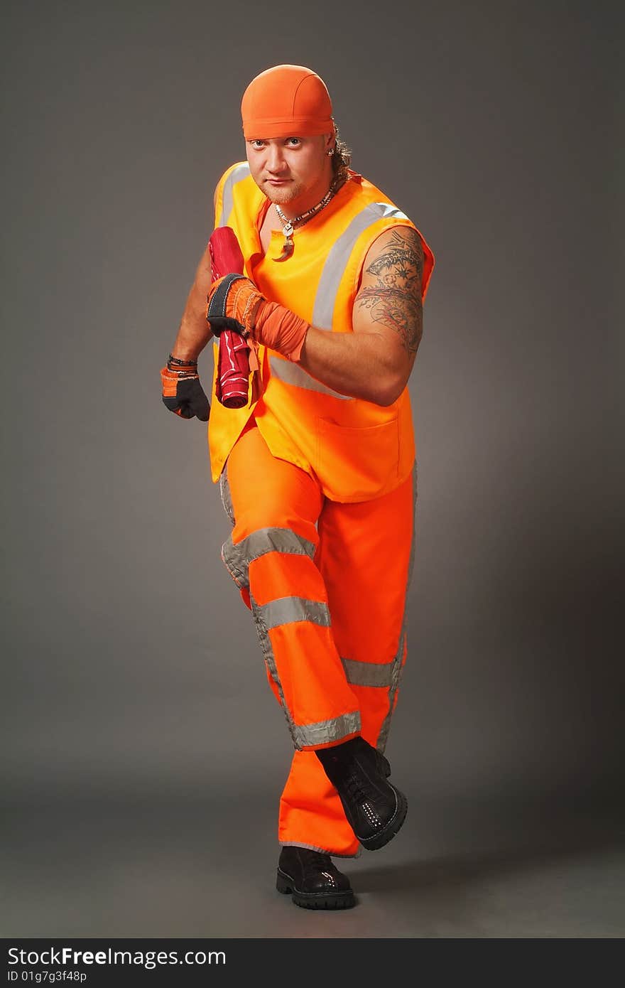 The worker in orange clothes on a grey background in studio. The worker in orange clothes on a grey background in studio