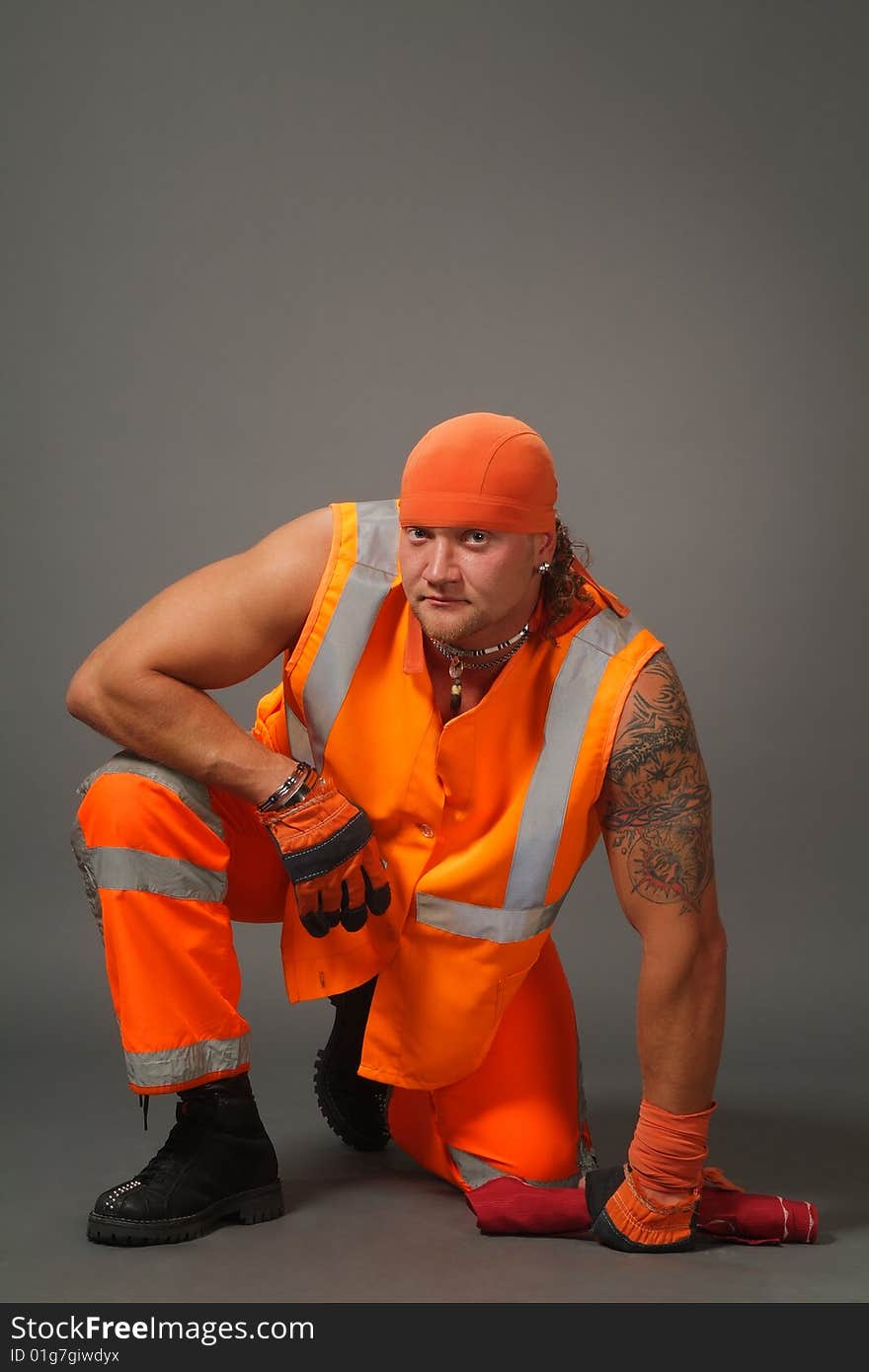 The worker in orange clothes on a grey background in studio. The worker in orange clothes on a grey background in studio