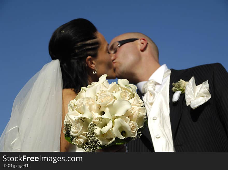 Bride and groom is kissing while showing their bouquet. Please note that the focus is on the flowers. Bride and groom is kissing while showing their bouquet. Please note that the focus is on the flowers.