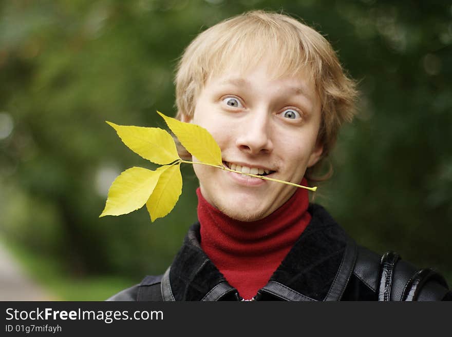 A young man with yellow autumn leaves in your teeth