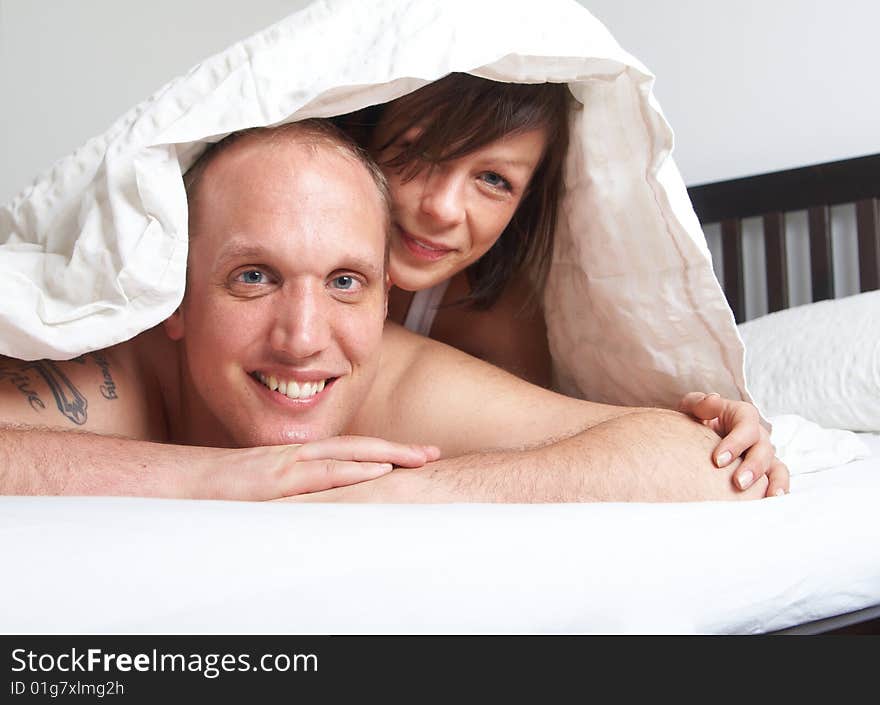 Young couple in their bed. They are playing in romance under the sheets. Young couple in their bed. They are playing in romance under the sheets.