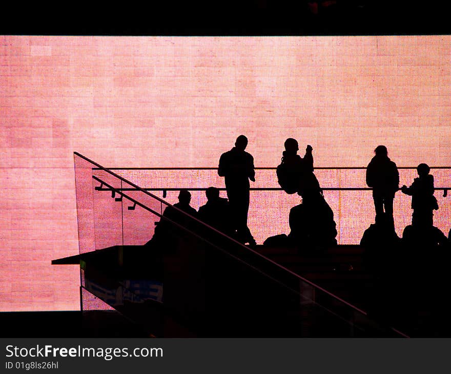 People silhouetted against huge video screen.