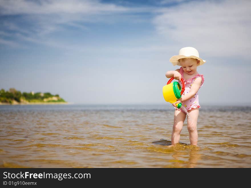 Small girl with watering-pot on the seashore