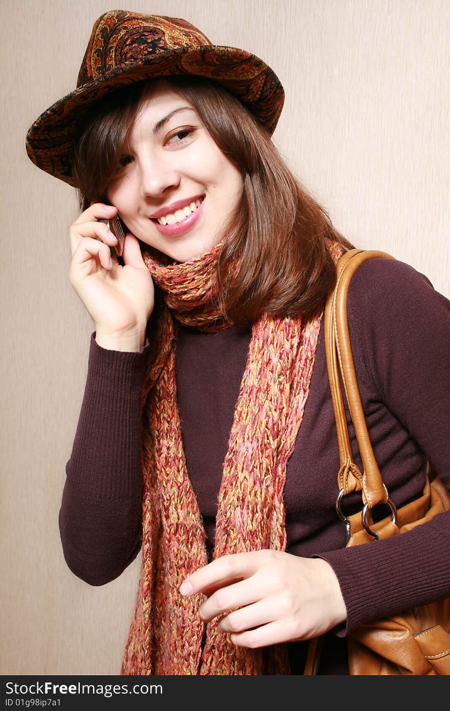 The girl in a felt hat and an orange scarf speaks by phone. The girl in a felt hat and an orange scarf speaks by phone.