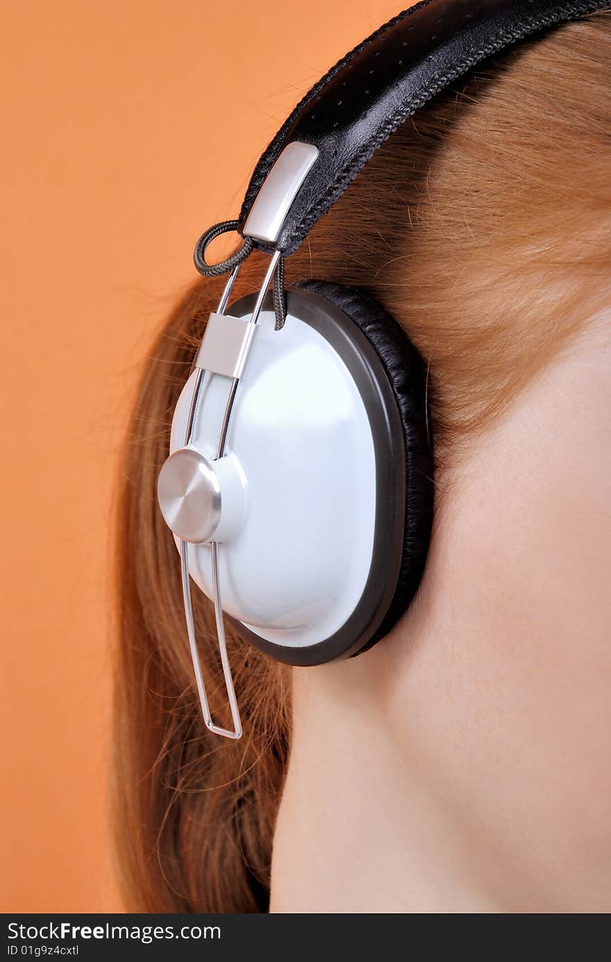 Redhead young woman in headphones on an orange background. Redhead young woman in headphones on an orange background