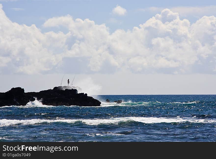 Silhouette of a fisherman on rocky headland off the coast of Kauai