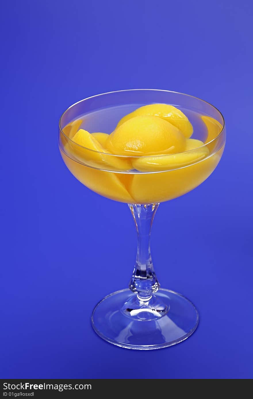 Halves of peaches in light syrup in a glass  on a dark blue background. Halves of peaches in light syrup in a glass  on a dark blue background