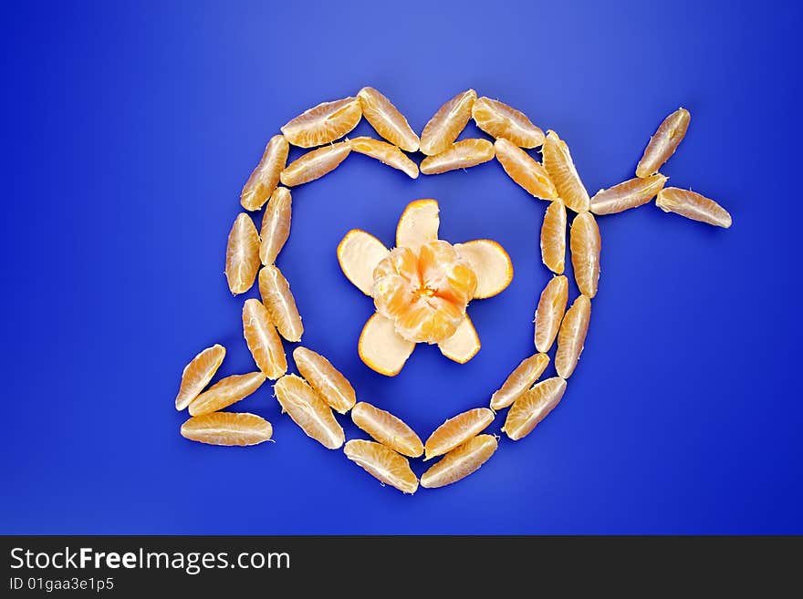 Slices of a tangerine stacked as the heart pierced with an arrow, on a dark blue background. The concept of love. Slices of a tangerine stacked as the heart pierced with an arrow, on a dark blue background. The concept of love.