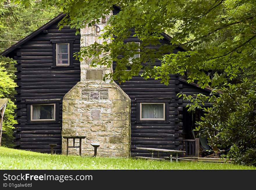 A log cabin side view, surrounded by trees in summer. A log cabin side view, surrounded by trees in summer