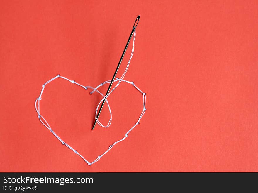 Needle standing on red background with embroidered heart