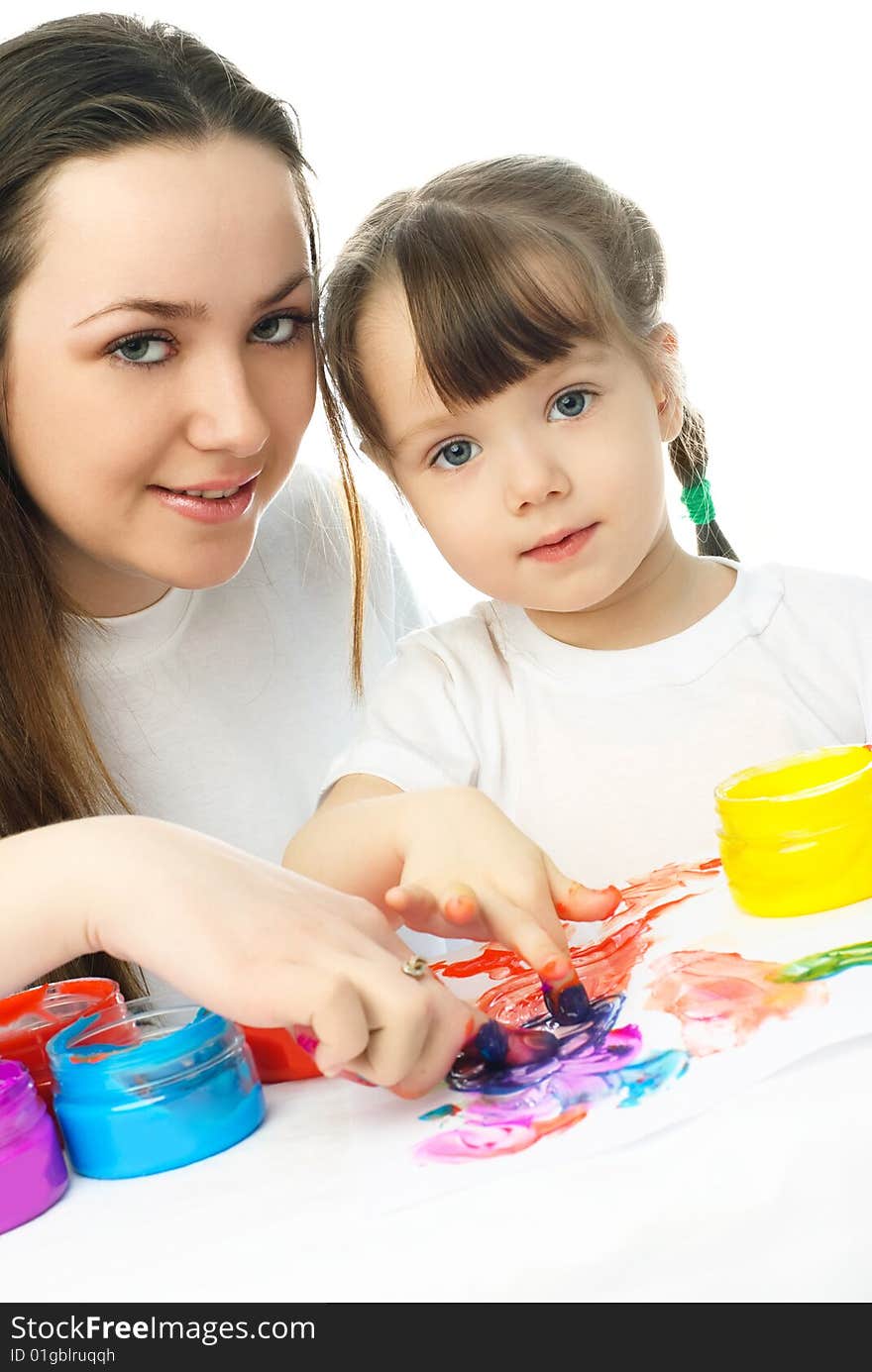 Young mother and her daughter sitting by the table and painting with finger paints. Young mother and her daughter sitting by the table and painting with finger paints