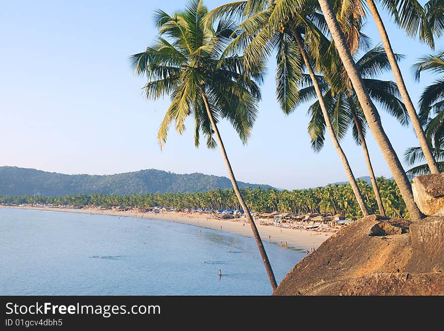 Palm trees with beautiful seascape on background with mountains, bay, sand beach and shacks. Palm trees with beautiful seascape on background with mountains, bay, sand beach and shacks.