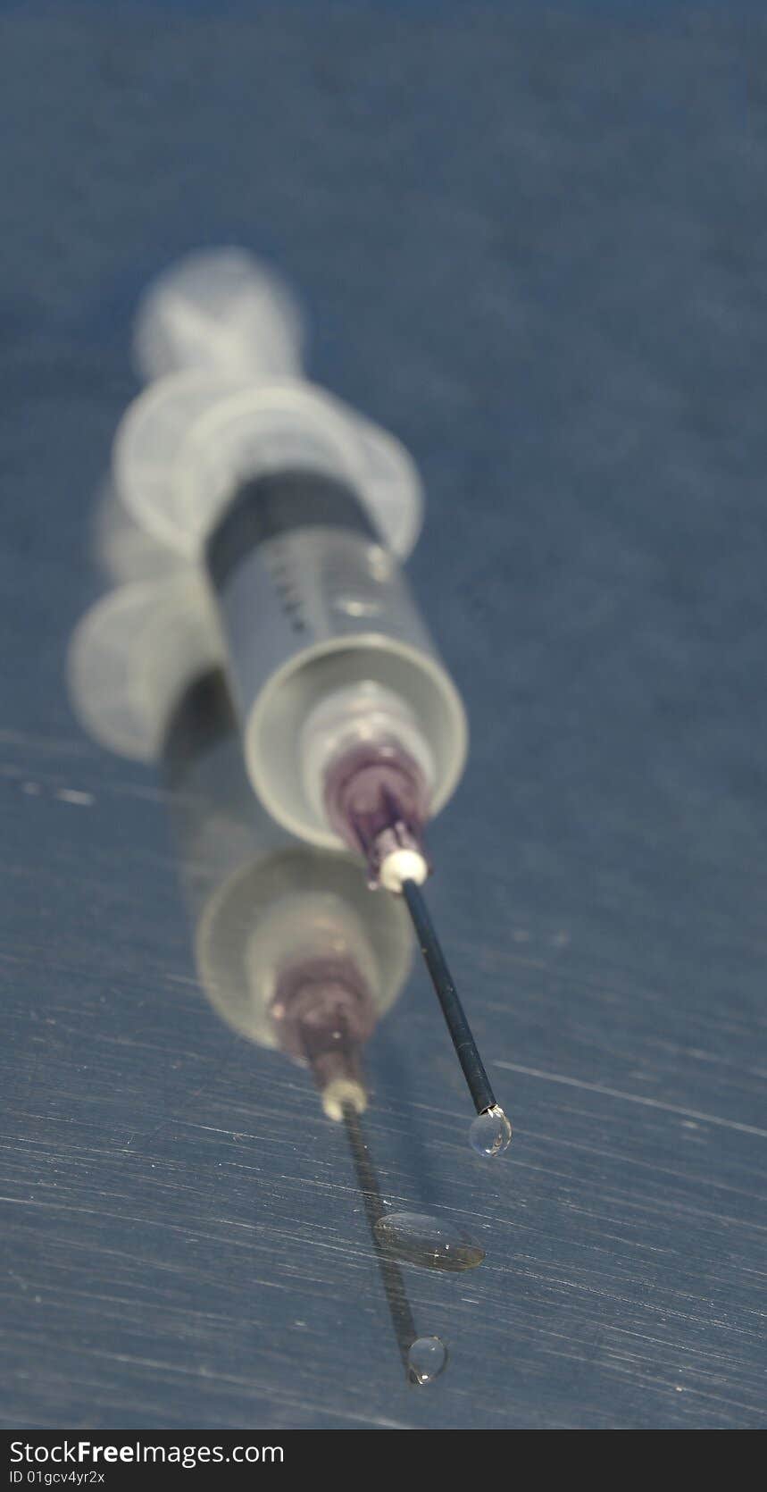 Syringe with sharp needle and little drop in shallow dof with focus on top of needle