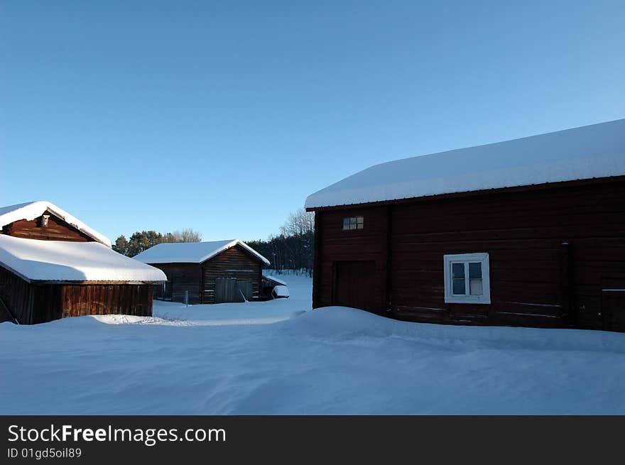 Swedish farm in winter, with barn and a clear blue sky.