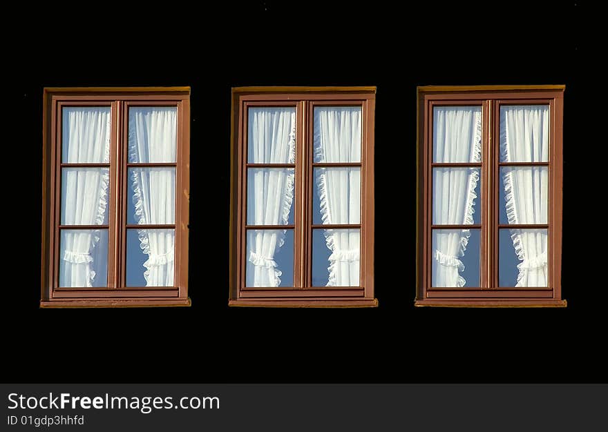 Three windows with white curtains in black background.