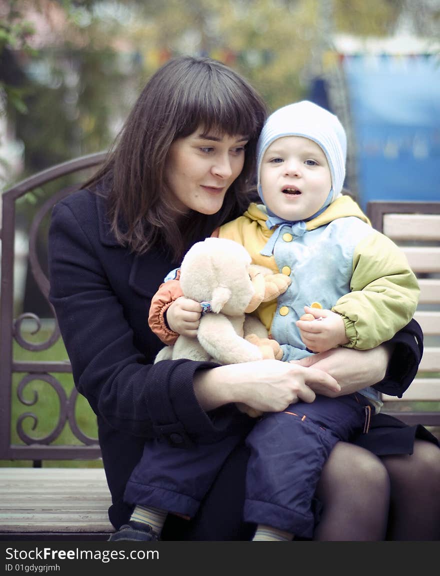 A young mother sitting on a park bench with her baby child in her arms. A young mother sitting on a park bench with her baby child in her arms.