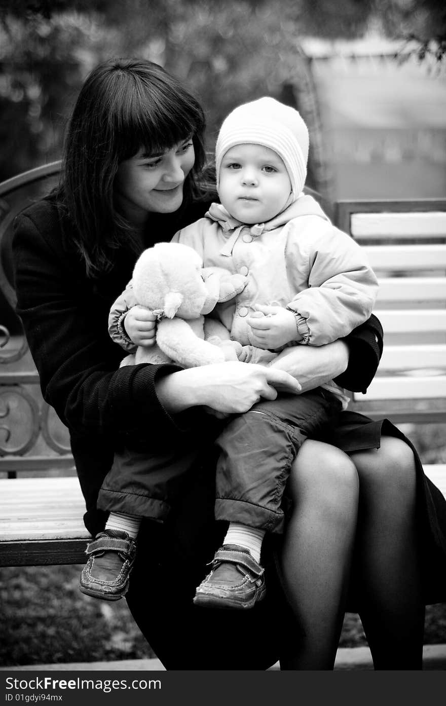 A young mother sitting on a park bench with her baby child in her arms. A young mother sitting on a park bench with her baby child in her arms.