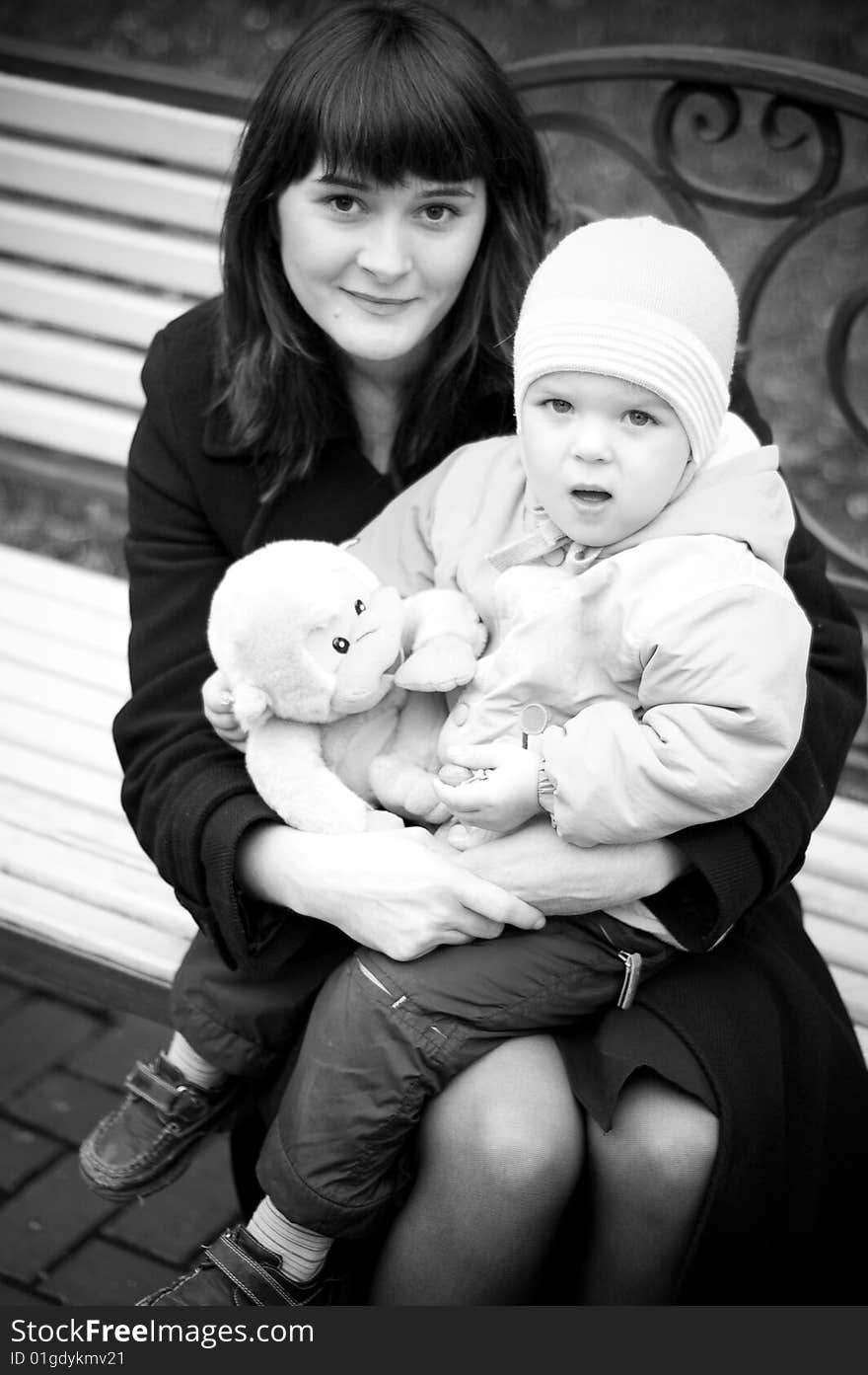 A young mother sitting on a park bench with her baby child in her arms. A young mother sitting on a park bench with her baby child in her arms.