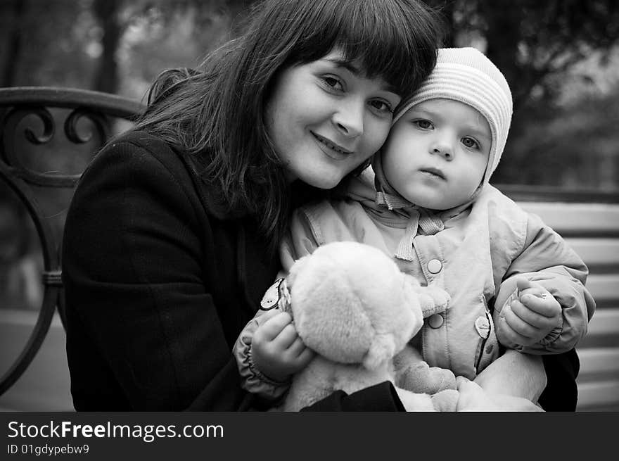 A young mother sitting on a park bench with her baby child in her arms. A young mother sitting on a park bench with her baby child in her arms.