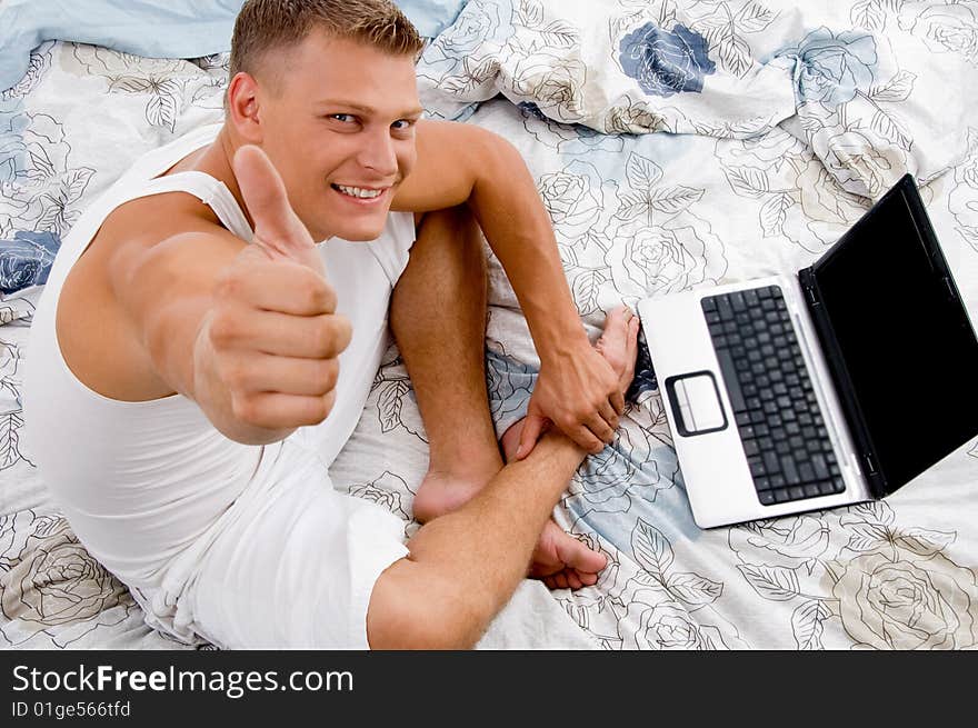 Young man with thumbs up and laptop in bed