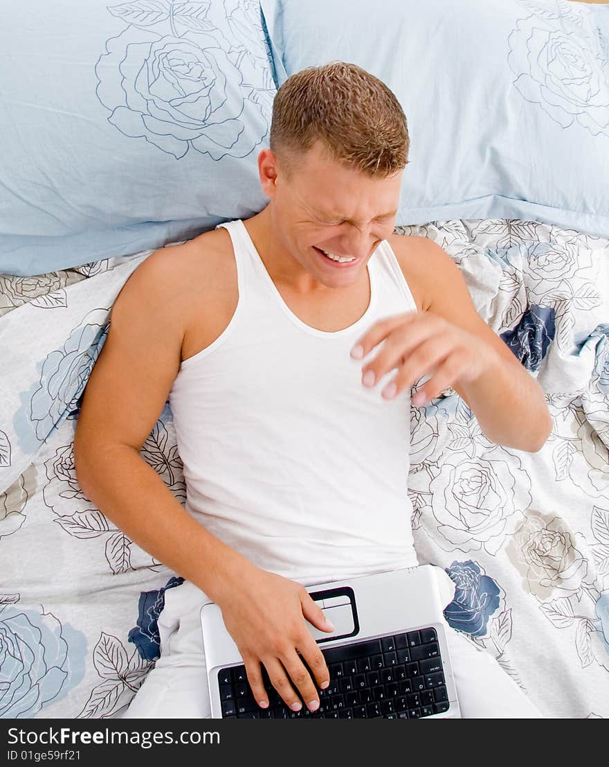 Young man with his notebook with facial expressions in bed. Young man with his notebook with facial expressions in bed