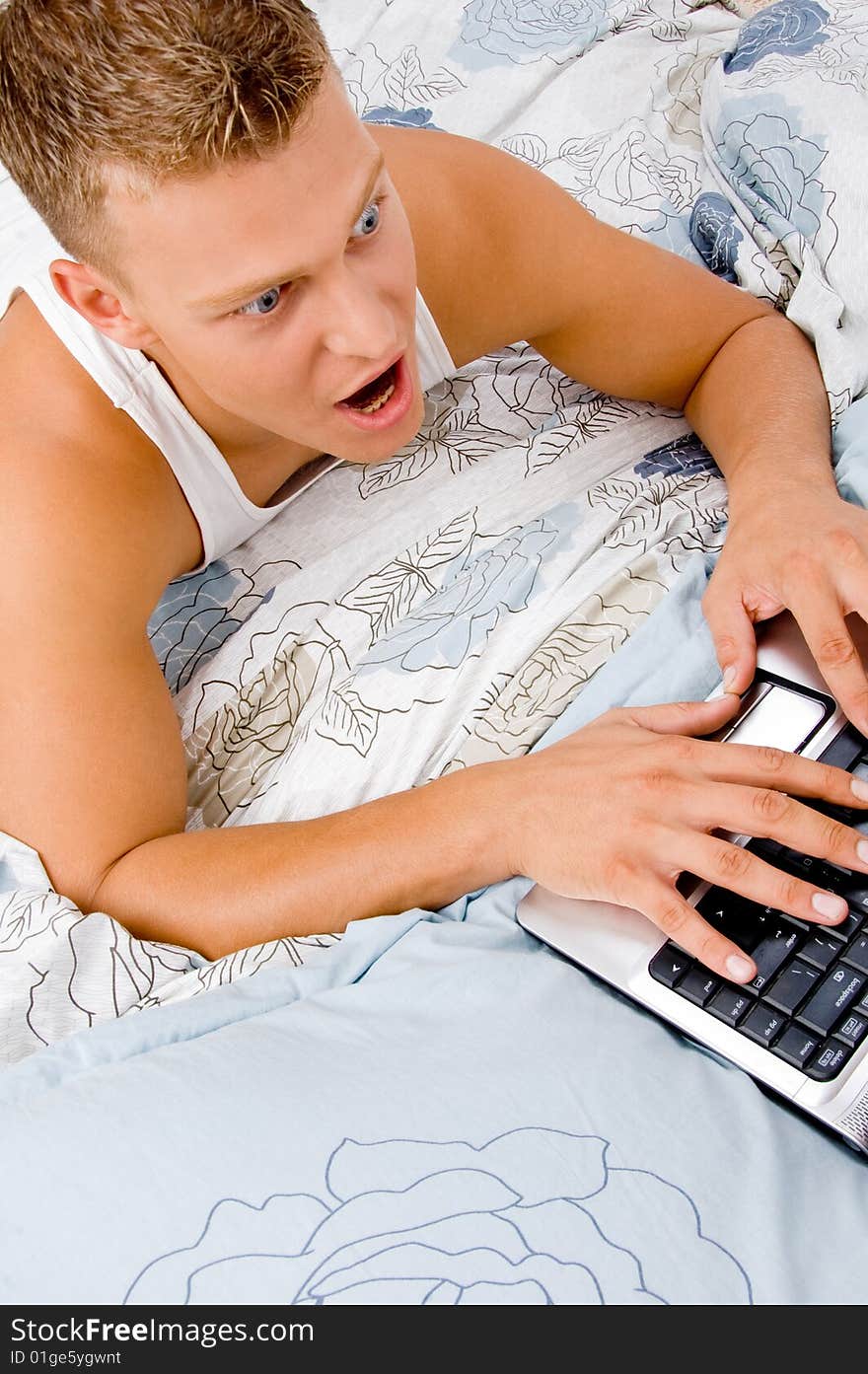 Handsome man working on laptop at home in bed. Handsome man working on laptop at home in bed