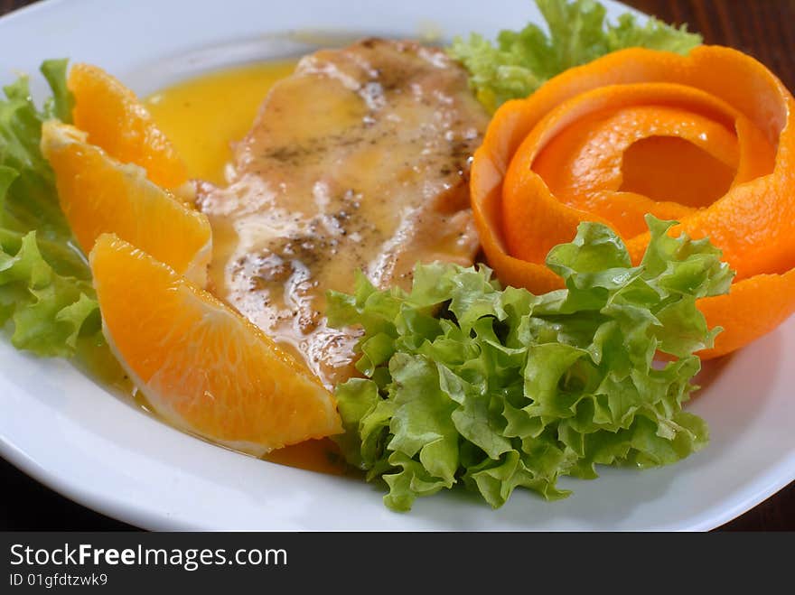 A plate of juicy pork chop with green salad, decorated with slices of orange and citron shaped as a rose. A plate of juicy pork chop with green salad, decorated with slices of orange and citron shaped as a rose