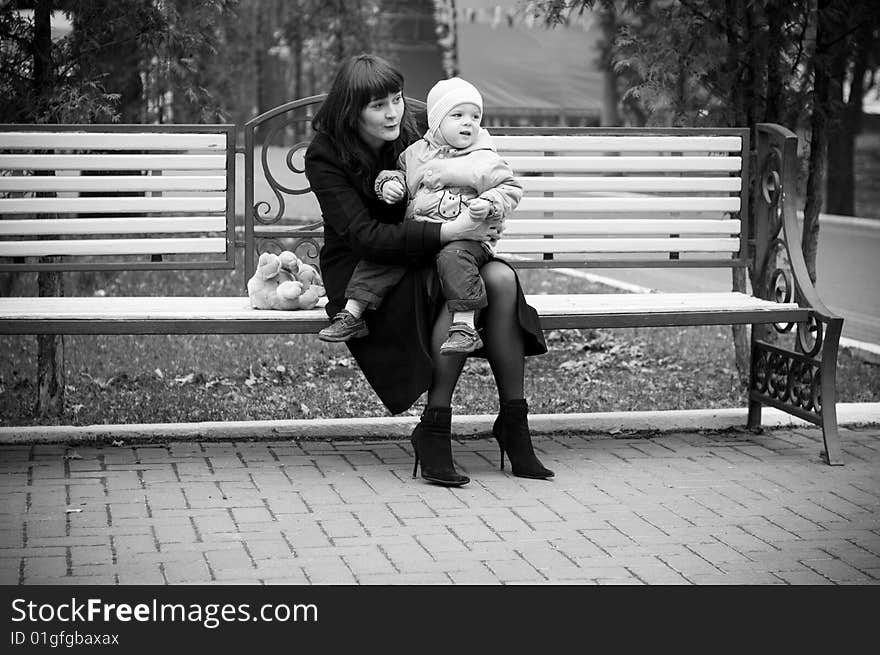 A young mother sitting on a park bench with her baby child in her arms. A young mother sitting on a park bench with her baby child in her arms.