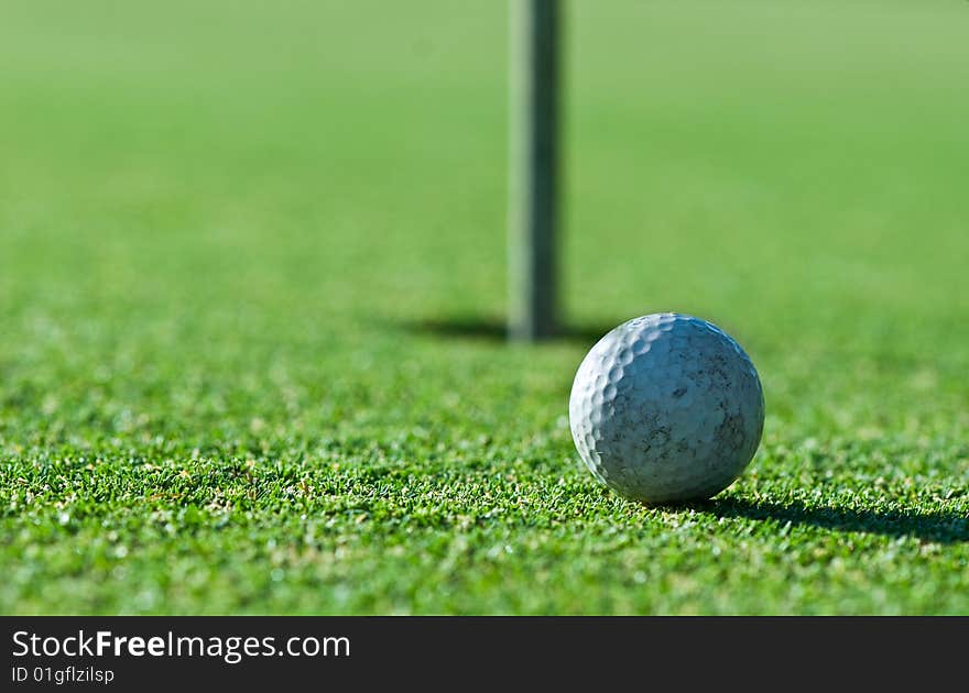 A close up of an old scuffed up golf ball on the green with the hole and flag in the background. Narrow depth of field. A close up of an old scuffed up golf ball on the green with the hole and flag in the background. Narrow depth of field.