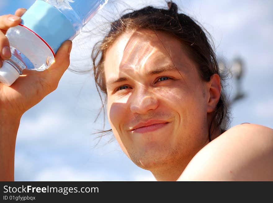 Smiling young man holding a plastic bottle with the water; light is passing through the bottle and it gives amusing shadow on the young man's face :-)). Smiling young man holding a plastic bottle with the water; light is passing through the bottle and it gives amusing shadow on the young man's face :-))