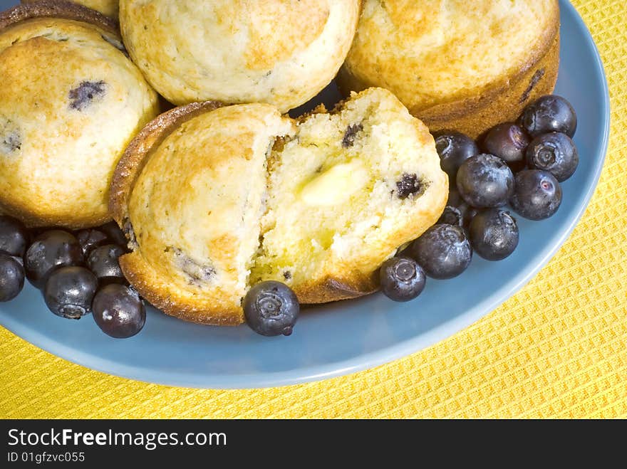 Fresh Blueberry Muffins with melting butter on a blue plate with yellow background  copy space. Fresh Blueberry Muffins with melting butter on a blue plate with yellow background  copy space