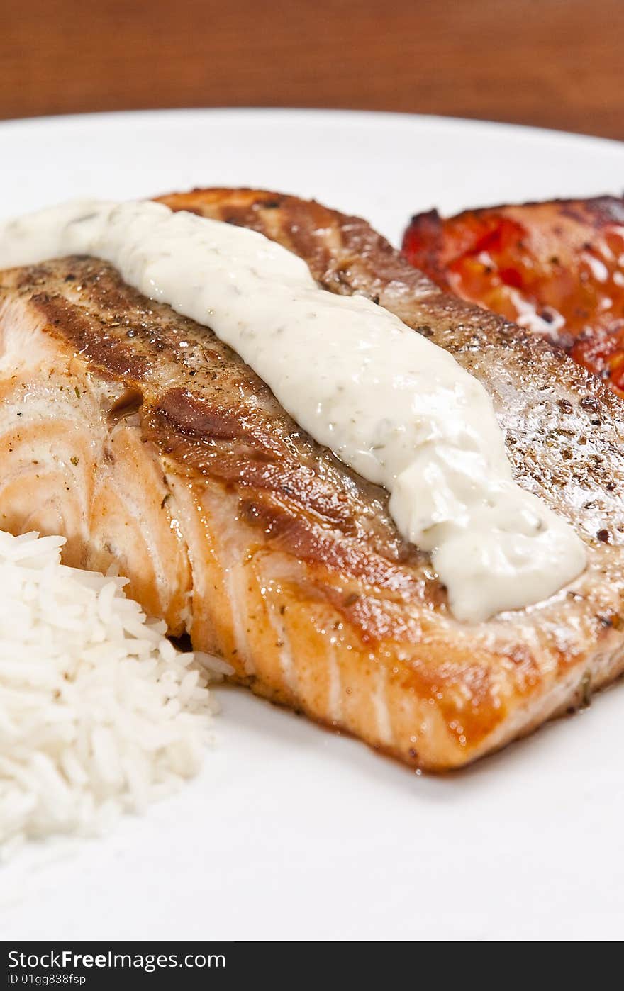 Cooked salmon fillet on white plate with rice and tomato