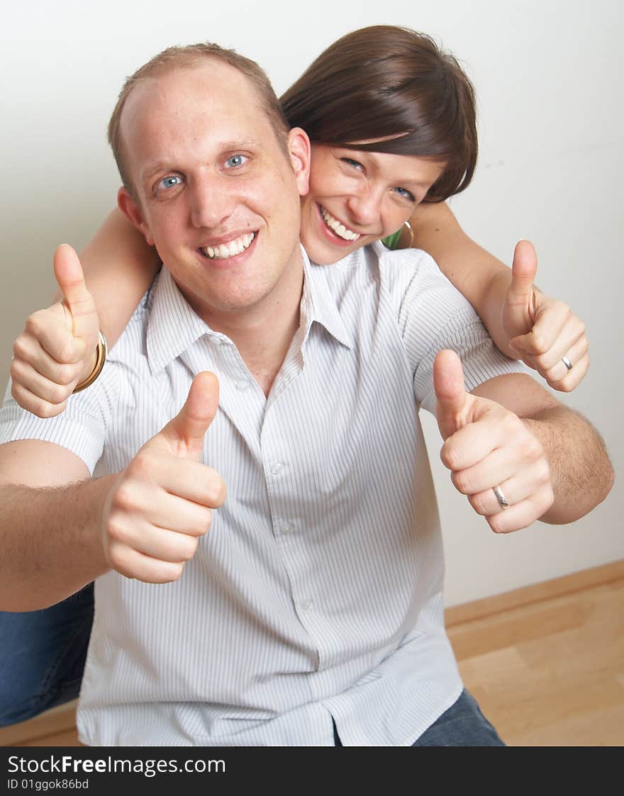 A young couple in love shows a thumbs up sign in their new appartment.