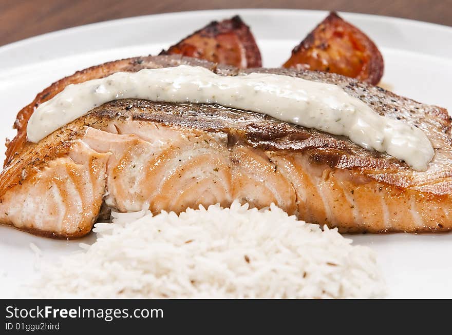 Cooked salmon fillet on white plate with rice and tomato